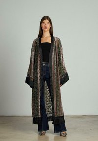 Kimono lung cu un model colorat, cu nuanțe vibrante, având tivuri din franjuri negri și un guler asemănător satinului. Purtați peste un top negru ajustat și blugi evazați.
