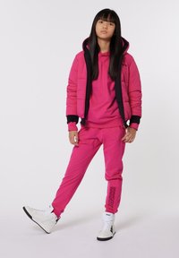 Chaqueta acolchada rosa con detalles negros, sudadera con capucha rosa a juego y pantalones de chándal, zapatillas altas blancas con detalles negros, textura suave.