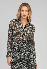 Chemisier transparent noir et blanc avec un devant à boutons, présentant un design texturé et fluide, des manches longues et un col.