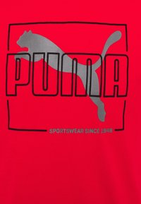 Rød T-shirt lavet af bomuld med et stort gråt Puma-logo og tekst. Omrids i sort, med "SPORTSWEAR SINCE 1948" nederst.