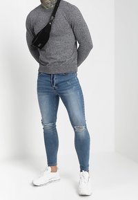 Grå långärmad tröja, blå slitna skinny jeans, svart axelväska och vita sneakers. Avslappnad outfit med en strukturerad stickning och denimfinish.