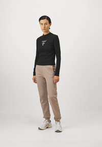 Sort langærmet skjorte med "GUESS" logo; beige joggebukser med mønstrede sidest stripes; parret med hvid og grå sportssko.