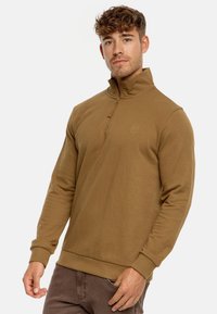 Brun fleece pullover med høj krave, halvlås foran og elastiske manchetter. Har et lille logo på brystet og en blød tekstur.