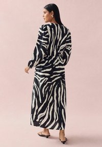 Robe maxi à motif zèbre noir et blanc avec de longues manches bouffantes et une taille cintrée, réalisée en tissu léger. Portée avec des sandales minimalistes.
