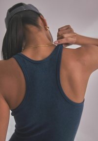 Tume sinine soonikko tank top laiemate rihmadega, millel on tekstureeritud muster ja väike embosseeritud logo seljal kaeluse lähedal.
