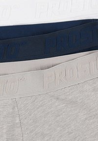 Trzy pary bielizny ułożone jedna na drugiej: biała, granatowa i szara. Każda z nich ma teksturowany elastyczny pas z wyembossowanym napisem „PROSTO” w dopasowanych kolorach.