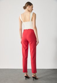 Haut blanc ajusté avec de larges bretelles et un dos nu, associé à un pantalon rouge taille haute arborant une silhouette épurée et une fermeture éclair à l'arrière.