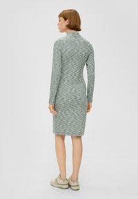 Dzianinowa sukienka w jasnym zielonym kolorze z prążkowaną teksturą, długimi rękawami, stójką i sylwetką do kolan. W zestawieniu z jasnymi sneakersami.