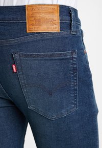 Mörkblå denimjeans med en läderetikett på baksidan, med en klassisk femficksdesign och ett subtilt sömmönster på fickorna.