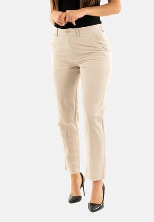 Pantalones beige de corte ajustado con pasadores para cinturón, bolsillos frontales y piernas ligeramente entalladas, acompañados de zapatos de tacón alto negros.