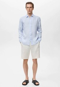 Camisa de lino de botones azul claro, pantalones cortos de lino crema y sandalias negras. Diseño simple con un corte relajado y texturas suaves.