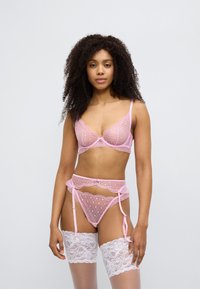 Σετ ροζ δαντελωτών εσωρούχων που περιλαμβάνει διάφανο σουτιέν με κυματιστά άκρα, ζώνη για καλσόν που ταιριάζει και λευκές δαντελωτές κάλτσες με ανθικά σχέδια.