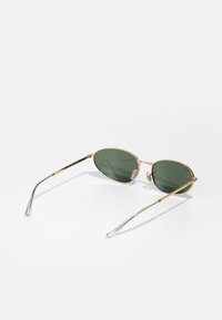 Gafas de sol con marco dorado y lentes verdes, de forma ovalada y con puntas transparentes en las patillas. Diseño de metal ligero con almohadillas nasales ajustables.