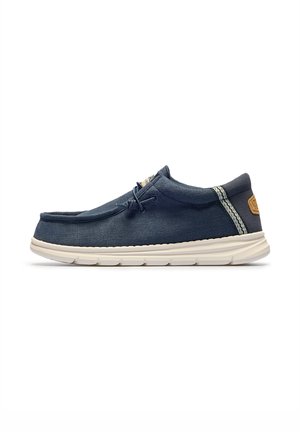 Zapato casual de hombre en azul marino con suela blanca, detalle de cordones y pestaña de tela con patrón en el talón, mostrado en perfil lateral.