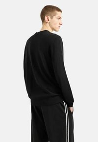 Felpa nera con maniche lunghe e polsini a costine, con un design a girocollo. Texture liscia, abbinata a pantaloni della tuta neri con strisce bianche.
