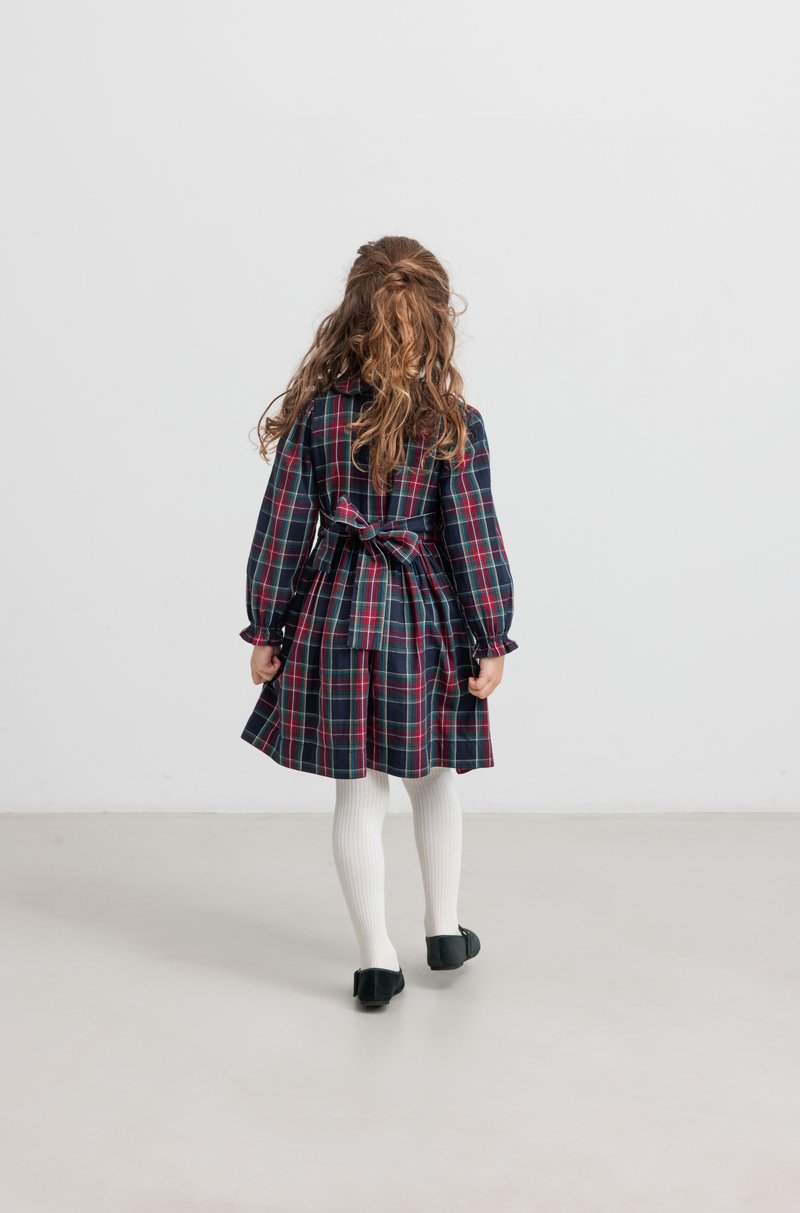 Καρό φόρεμα με μακριά μανίκια και ζώνη στη μέση, με σκούρους μπλε, κόκκινους και πράσινους σχεδιασμούς. Λευκές ριπτές καλσόν και μαύρα παπούτσια.