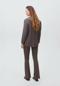Blazer à carreaux marron, coupe ajustée, associé à un pantalon en flanelle marron évasé. La tenue présente une texture subtile et des fentes latérales au niveau des pantalons.