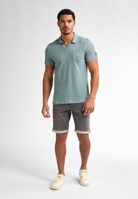 Svetle tyrkysové polo tričko s kapsou na prsou, spárované s šedými džínovými šortkami s ohrnutými lemy a bílými teniskami. Jednoduchý design, krátké rukávy.