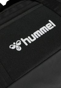 Black backpack with textured fabric, featuring a prominent white "hummel" logo and a distinct honeycomb graphic on the front.