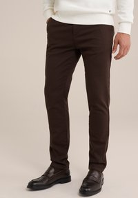 Chino de bumbac maro cu croială slim și buzunare laterale, asortați cu loaferi maro închis. Țesătura are o textură netedă și o culoare uniformă.