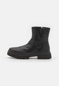 Botas negras hasta el tobillo hechas de cuero suave con una suela gruesa y estriada, que presentan dos hebillas laterales y un diseño de punta redondeada.