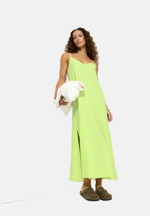 Robe maxi vert clair avec des bretelles spaghetti, une fente sur le côté et une coupe aérienne, associée à des chaussures slip-on marron foncé.