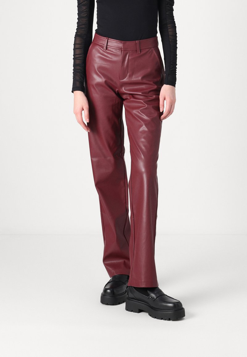 Pantalons en cuir bordeaux à taille haute, jambes droites et poches latérales, associés à des mocassins noirs à semelles épaisses.