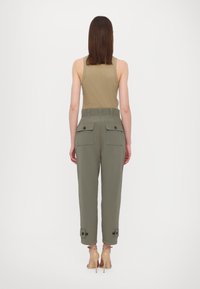 Sleeveless, olive green top paired with high-waisted, tapered cargo pants featuring two back pockets, button accents, and cuffed hems.