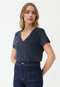 Granatowa koszulka z dekoltem w serek, wykonana z gładkiego materiału, z krótkimi rękawami i luźnym krojem, połączona z ciemnoniebieskimi jeansami typu high-waist z złotymi przeszyciami.