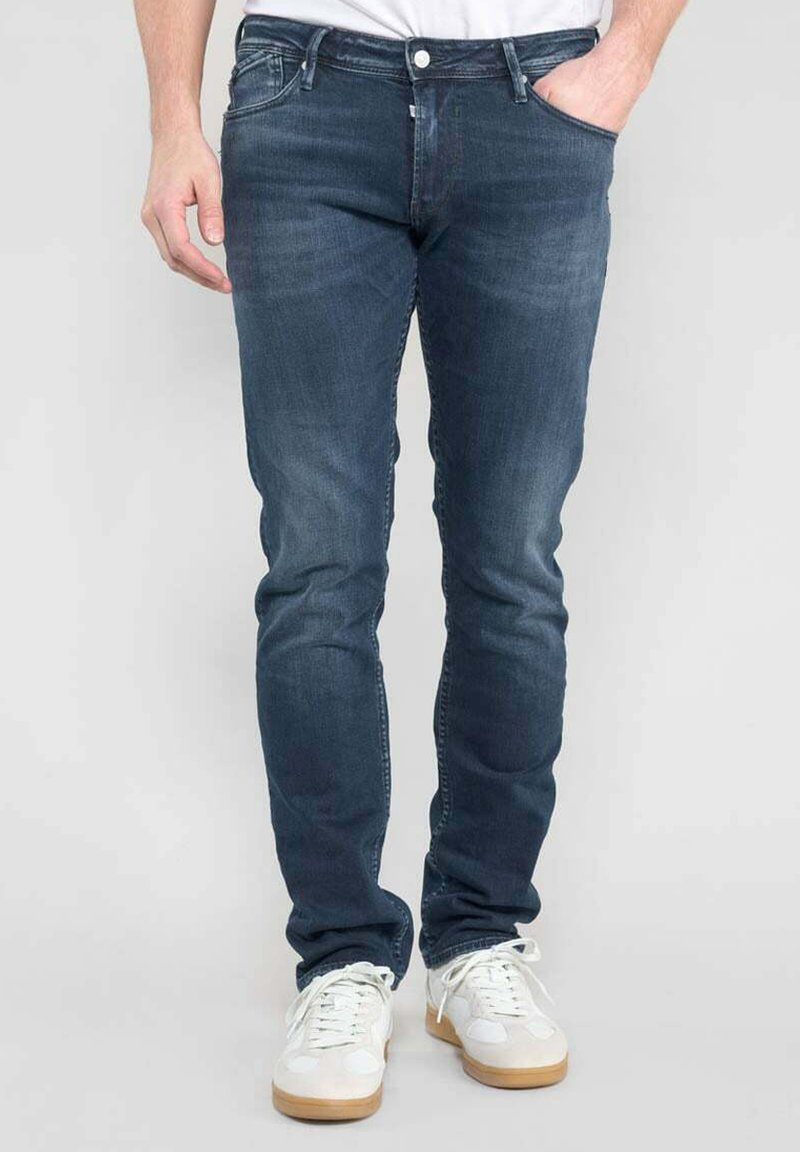 Jeans en denim bleu foncé avec une coupe slim, dotés de cinq poches et de détails légèrement décolorés. Portés avec des baskets blanches et un t-shirt uni.