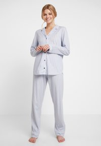 Blå randig pyjamas med lång ärm, knappar och lösa byxor; mjukt tyg och avslappnad passform. Accentuerad med subtila gula ränder.
