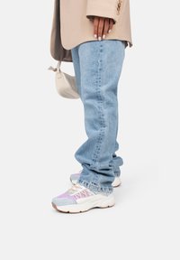 Jean en denim bleu clair avec une coupe décontractée, associés à des baskets multicolores avec une tige violette et bleu clair et une semelle blanche.