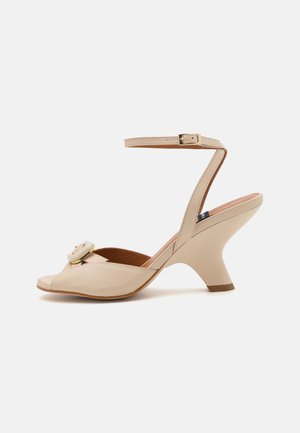 Beige leather ankle-strap shoe with a peep toe, featuring a decorative buckle and a mid-height, curved heel. Smooth texture and structured design.