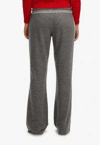Grå, vide joggingbukser lavet af blødt stof. Har en bred taljebånd med en subtil kontrastdetalje. Glat tekstur og afslappet pasform.