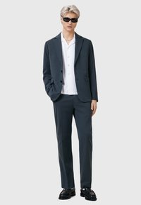 Ciemnoszary garnitur składający się z dopasowanej marynarki i pasujących spodni, w połączeniu z białą koszulą na guziki oraz czarnymi okularami przeciwsłonecznymi.