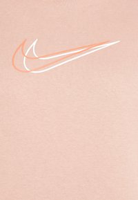 Persikofärgad t-shirt med en stor Nike Swoosh-logotyp i vitt och ljusorange. Tillverkad av mjukt, texturerat tyg med rundad hals.