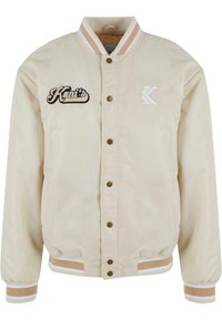Beige Bomberjacke mit zwei vorderen Taschen, Druckknöpfen, gerippten Bündchen und Kragen. Mit aufgesticktem "Kani's Diner" und Logo-Detail.