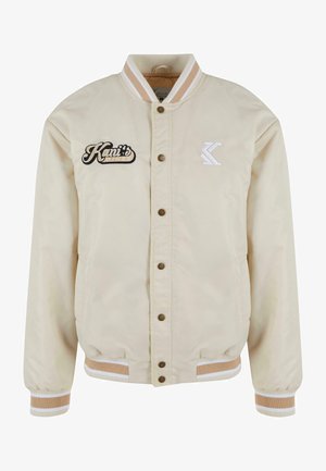 Beige bomberskinnjakke med to frontlommer, trykknapper, ribbestrikkede mansjetter og krage. Har broderte detaljer med "Kani's Diner" og logo.
