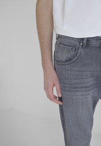 Jeans de mezclilla gris con un acabado ligeramente desgastado, que cuentan con una etiqueta en el bolsillo trasero que dice "HORATO". La tela tiene una textura suave.