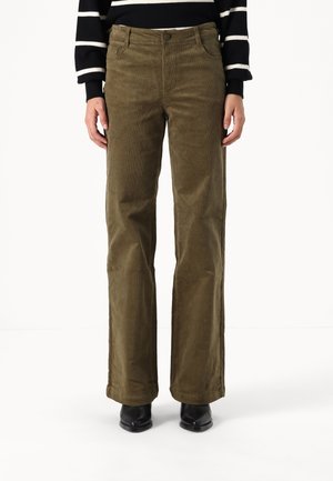 Osoba ubrana w oliwkowozielone, sztruksowe spodnie o prostych nogawkach, czarne botki za kostkę oraz czarno-biały, paskowany sweter.