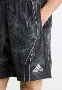 Shorts neri con un motivo grigio a spirale, vita elastica con tasche e un notevole logo bianco Adidas sul lato inferiore sinistro.