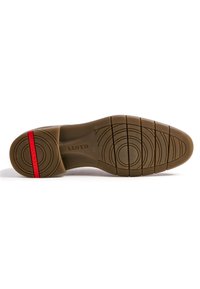Semelle d'une chaussure en caoutchouc beige, présentant des motifs de semelle circulaires et linéaires, avec une bande d'accent rouge près du talon.