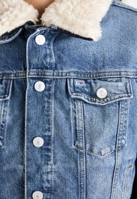 Chaqueta de mezclilla con un lavado azul claro, cuello de faux fur texturizado, broches metálicos y dos bolsillos en el pecho con un sutil detalle de logo.