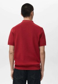 Polo rossa a maniche corte con motivo a maglia strutturata, colletto e vestibilità comoda, abbinata a pantaloni in denim scuro. Vista posteriore.