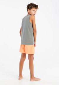 Grijze mouwloze shirt met een ontspannen pasvorm, gecombineerd met perzikkleurige shorts met een achterzak en een klein knoopdetail.