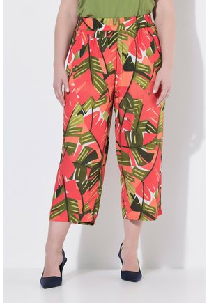 Wide-leg cropped pants with bright red and green tropical leaf pattern worn with navy pointed heels on a standing person.