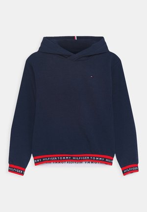 Mørkeblå hættetrøje med røde, hvide og mørkeblå ribkanter med logo på ærmer og kant, lille logo på brystet og korslagt hættedesign.