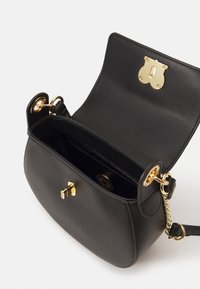 Sac à main en cuir noir avec une texture lisse, quincaillerie dorée, fermeture à verrou en haut et accent en chaîne sur la sangle. Intérieur visible.