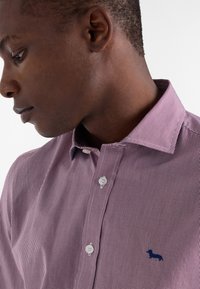 Camicia da uomo con bottoni in un motivo a quadri rosso e bianco, con colletto a punta e piccolo logo di un cane navy sul petto. Chiusura frontale con bottoni.