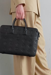 Malette en cuir noire avec le logo MCM embossé, de forme rectangulaire, deux poignées courtes et une texture à motif de diamant subtil.